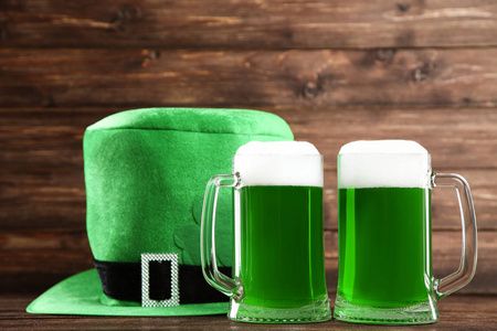 s Day. Green beer in mugs with hat on wooden background