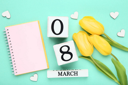 s Day on wooden calendar with yellow tulips and notepad