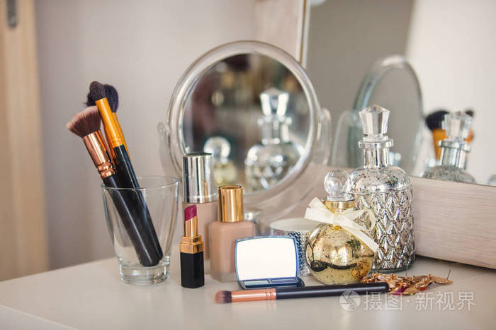 化妆艺术家香水,刷霜和其他化妆品与玫瑰近镜子在桌子上.