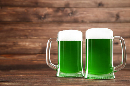 s Day. Glass mugs with green beer on brown wooden background