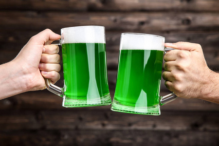 s Day. Glass mugs with green beer in male hands on wooden backgr