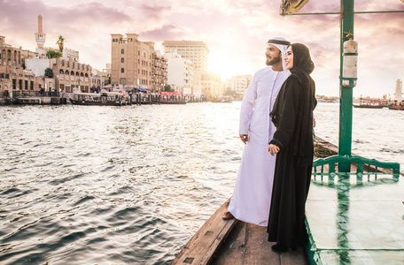 快乐的夫妇在迪拜度过时光。 男人和女人穿着传统的衣服在河上巡游