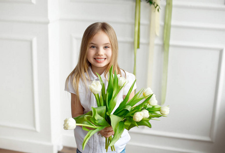 一个穿白色衬衫的漂亮小女孩的肖像，她很惊讶，手里拿着一束郁金香。
