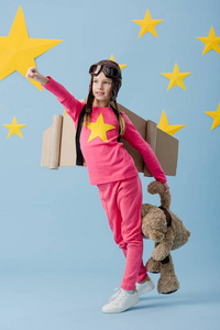 飞行头盔上的小孩滑稽地在蓝色星空背景上摆着玩具熊