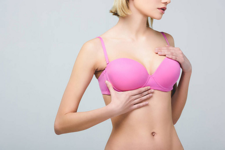 从灰色乳腺癌概念中分离出的粉红色胸罩中年轻女性的裁剪视图
