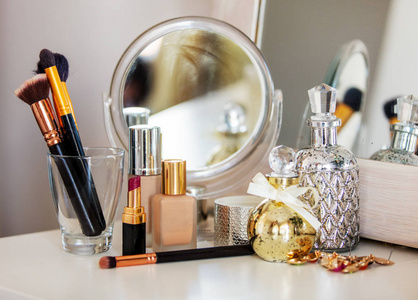 化妆艺术家香水，刷霜和其他化妆品与玫瑰近镜子在桌子上。