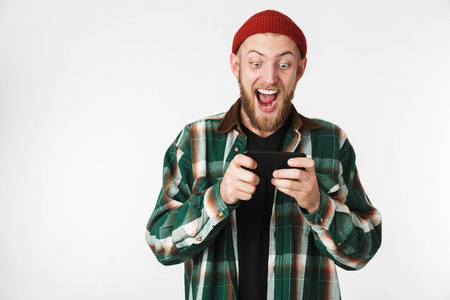 欧洲男子戴着帽子和格子衬衫，在手机上玩电子游戏，而在白色背景下孤立地站着。