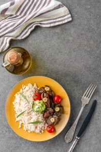 米饭肉和西兰花的顶部视图，盘子里有油叉子和刀