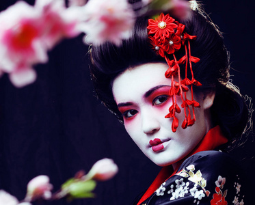 年轻漂亮真正的艺伎在和服与樱花和装饰黑色背景