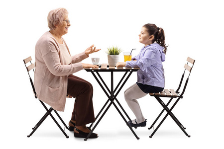 一位年长妇女坐在一张桌子旁喝咖啡，与她的孙女交谈，被孤立在白色背景下