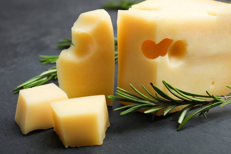 硬切片黄色马斯塔姆奶酪与迷迭香板上的黑色背景。 奶酪的概念。