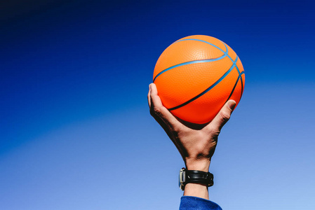 手拿一个橙色篮球球在蓝天背景邀请玩复制空间自由区。