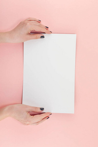 创意平躺顶部的女人手黑色指甲与空的A4纸页模拟在粘贴千禧粉纸背景复制空间。 最小写作概念模板的文字字母博客