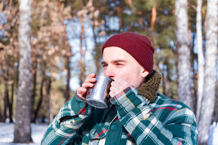 男人在一个下雪的冬天森林里从杯子里喝酒。 穿格子衬衫的男人在户外喝杯咖啡