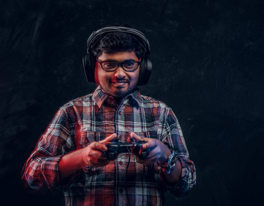 印度男子在无线耳机拿着操纵杆和玩电子游戏在控制台上站在演播室