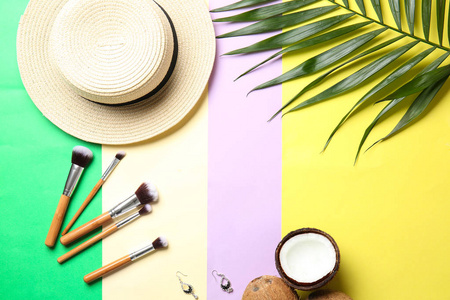 平躺构图与沙滩帽化妆刷和热带叶子的颜色背景