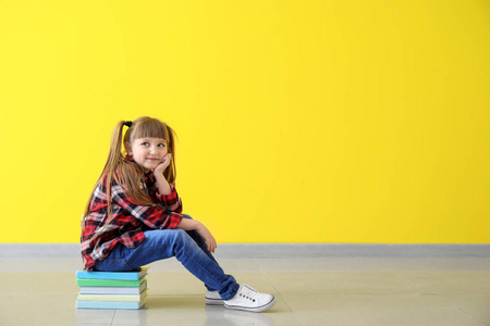 可爱的小女孩坐在一叠靠彩色墙的书上