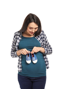 白色背景下带婴儿鞋的美丽孕妇肖像。
