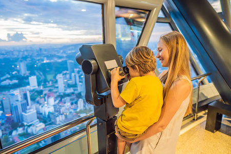 妈妈和儿子正在看瓜拉伦普尔的城市景观。使用双筒望远镜。在马来西亚的日落摩天大楼大楼里, 可以欣赏到吉隆坡城市天际线的全景。带孩子