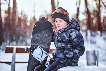 在冬天的森林里, 一个穿着雪衣的可爱小学生坐在长凳上的肖像