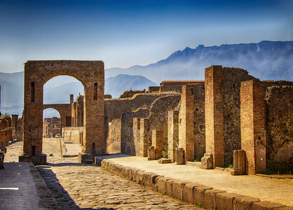 一扇石门和城市的废墟。 后面是蓝天和大山。 它位于欧洲的意大利庞培。