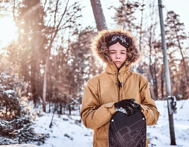 日落时分, 穿着暖和衣服的年轻滑雪者斜靠在雪地森林里的滑雪板上