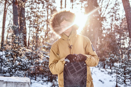 日落时分, 穿着暖和衣服的年轻滑雪者斜靠在雪地森林里的滑雪板上