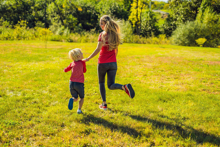 妈妈和儿子在绿草上跑步。 公园里的幸福家庭。