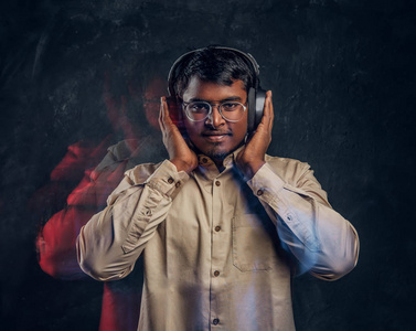 英俊的印度男人很高兴在黑暗的工作室里用无线耳机听音乐