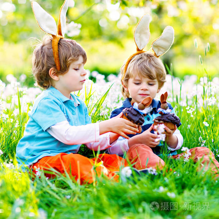 两个孩子的男孩和朋友在复活节兔子耳朵在传统的彩蛋狩猎在春季花园, 户外。兄弟姐妹吃巧克力蛋糕, 松饼和蛋糕。老基督徒和 cath