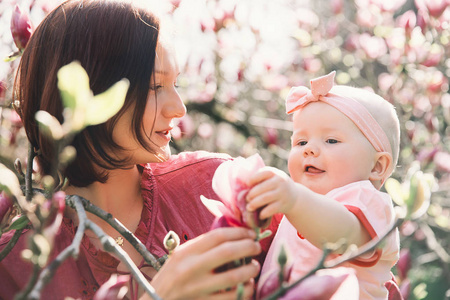 慈爱的母亲和女婴正在闻盛开的粉红色玉兰树。 年轻漂亮的妈妈和小女儿在户外的花园花中。 植物园自然的家庭