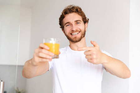 一个英俊的小胡子男人在家喝果汁，竖起大拇指。
