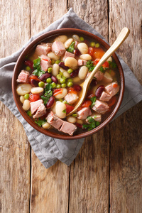 美味的豆汤，配上火腿西红柿和草药，放在桌子上的一个碗里。 垂直顶部视图，Abov