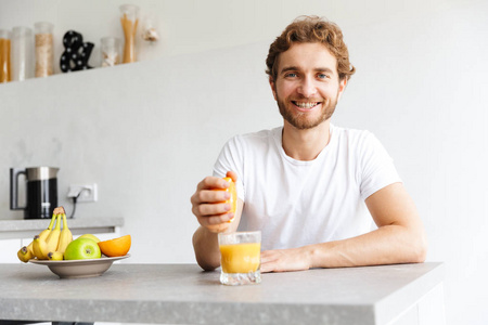 一个快乐的年轻留胡子的男人在家里的桌子上用水果做果汁的照片。