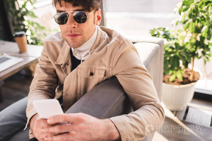 时尚男士戴墨镜在咖啡馆里使用智能手机