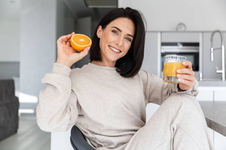 30岁的黑发女人在明亮的现代化房间里休息时喝橙汁