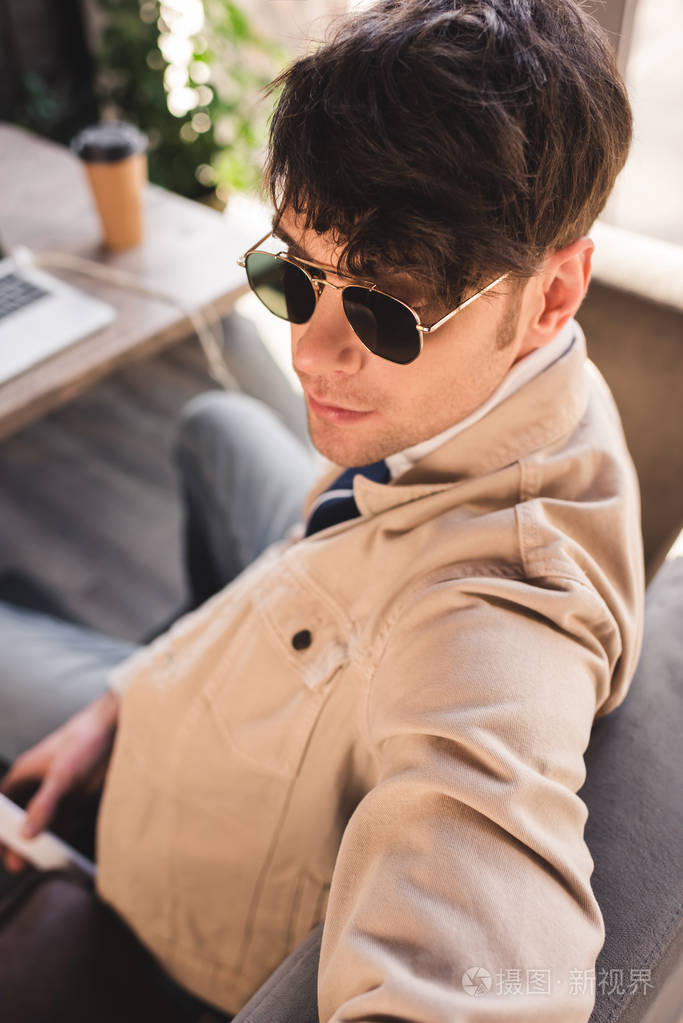 时尚男士戴墨镜坐在咖啡馆里的选择性专注