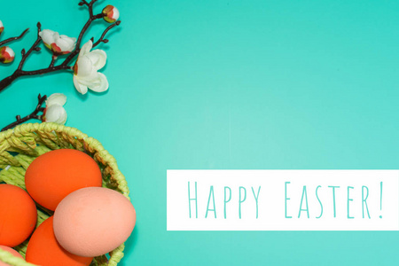篮子里有彩绘的鸡蛋和绿松石背景上盛开的树枝。 快乐复活节贺卡