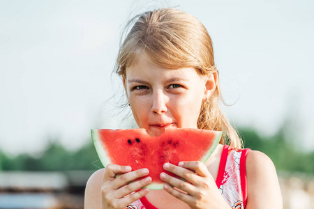 孩子在户外吃西瓜。 儿童健康零食。 小女孩拿着一片成熟的红西瓜