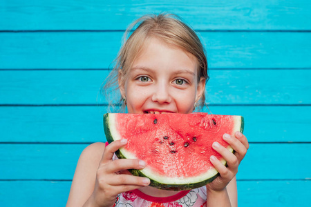 夏天，小女孩在蓝色的木板墙上吃成熟多汁的西瓜