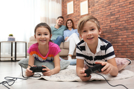 可爱的孩子在玩电子游戏，而父母则在家里沙发上休息