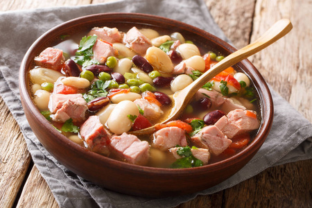 汤从豆子，豌豆，火腿，西红柿和草药在一个碗在桌子上特写。水平
