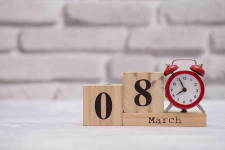 3月8日月8日在木制日历上，白色砖块背景上有红色闹钟。女人节快乐。