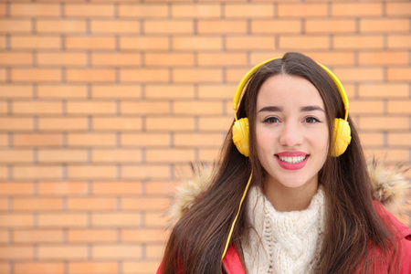 美丽的年轻女子用耳机听音乐靠在砖墙上。文本空间