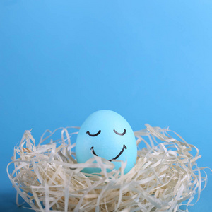 蓝色的鸡蛋，在巢的复制空间里涂上了微笑。 快乐复活节概念贺卡设计。