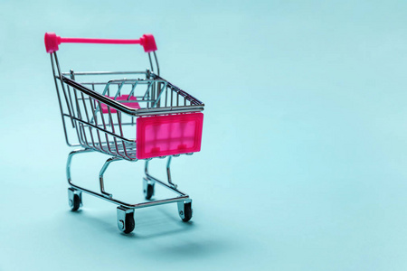 销售购买商场市场商店消费者概念。 小超市杂货店推车为购物玩具与车轮隔离在蓝色粉彩纸时尚背景。 复制空间