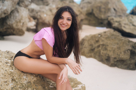 女孩的肖像在泳衣放松在海滩上与大石头在背景