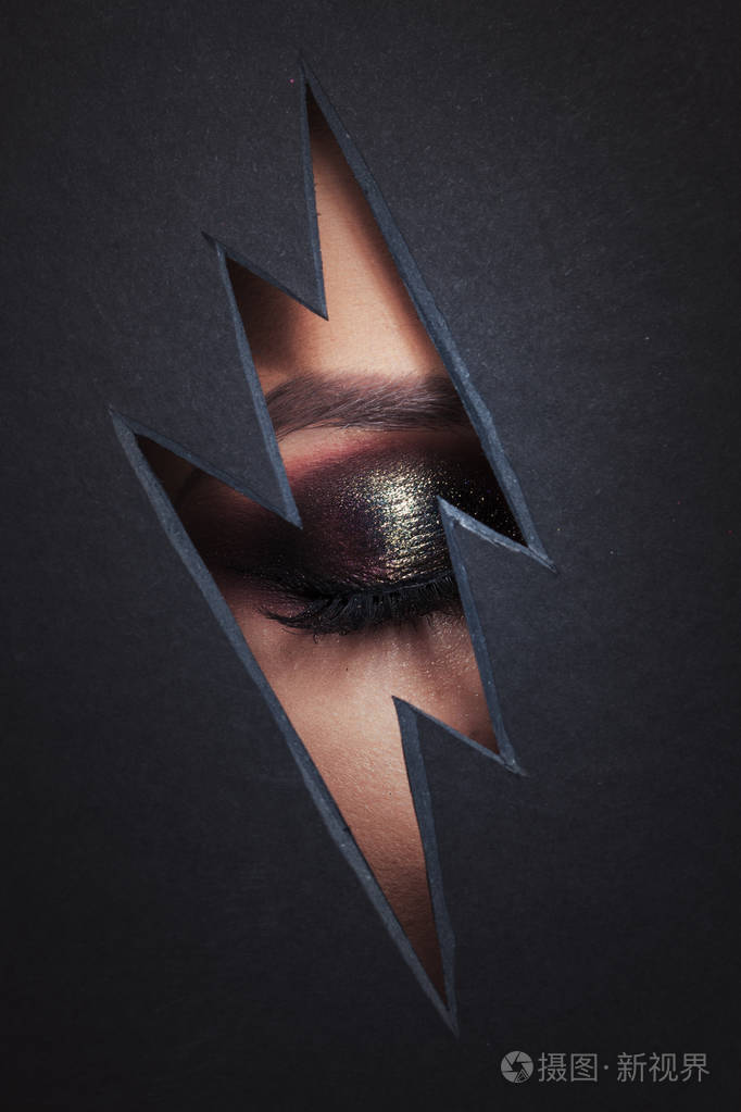 美丽的女性眼睛与彩妆以闪电的形式在纸上切割