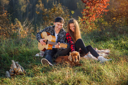 愉快的可爱的夫妇在休闲的衣服与吉他和他们的狗在野餐在公园里休息