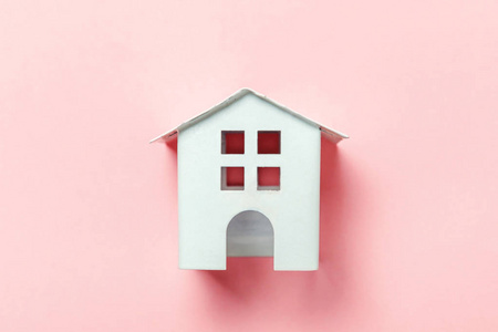 简单的设计与微型白色玩具屋隔离在粉红色粉彩彩色潮流背景。 抵押财产保险梦想家居概念。 平躺顶视复印空间